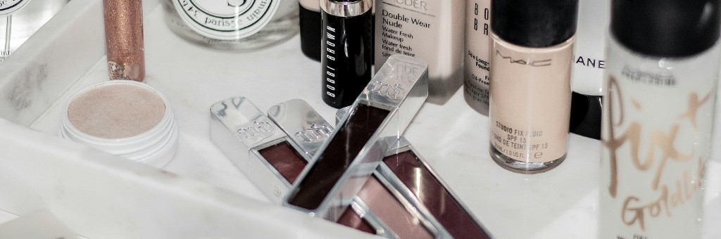 大理石の上に並ぶ MAC・Estée Lauder・Urban Decay などのラグジュアリーコスメ — 多様なブランドの並び